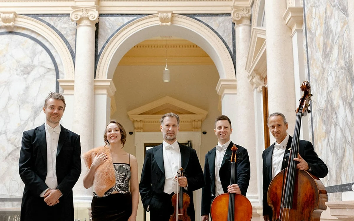 Five formally dressed musicians standing with string instruments and a flute