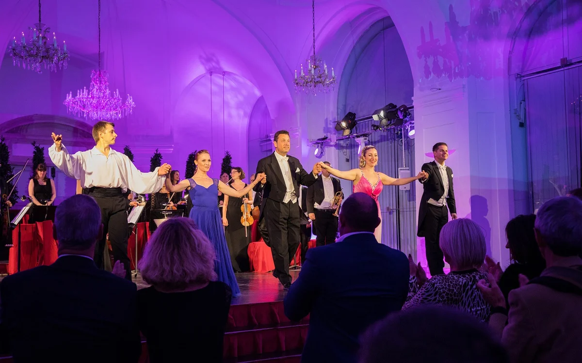 Musicians bowing after a performance in a room with chandeliers
